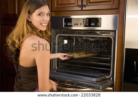 Young woman baking cookies placing pan in oven