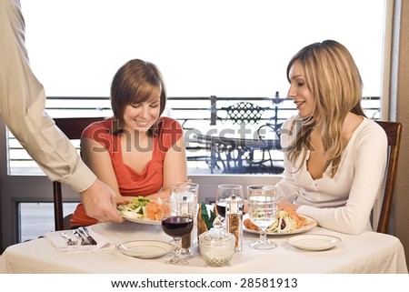 2 friends eating lunch at a cafe with a waiter brining food