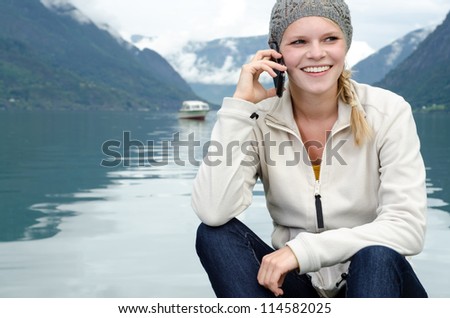 young blond woman called up with her Smartphone with a fjord in Norway in the background