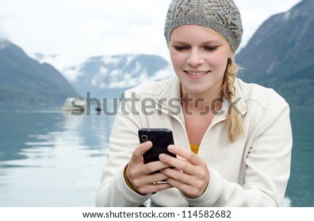 young blond woman with her Smartphone in the hand and a fjord in Norway in the background