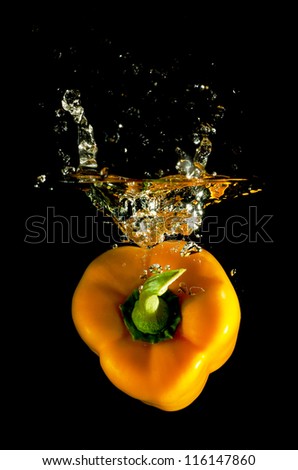 orange pepper falls in the water before black background