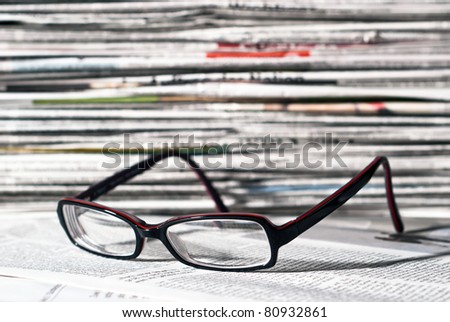 reading glasses lie before a big newspaper pile