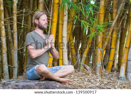 Attractive man doing yoga in an outdoor bamboo garden with copy-space. Hands in prayer pose.