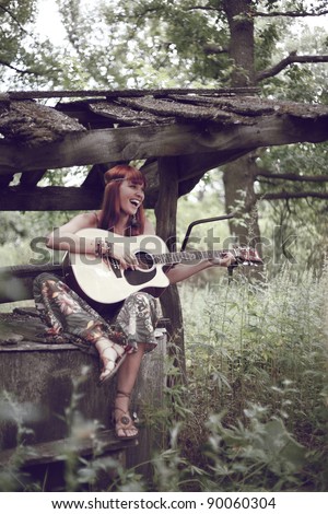 The cheerful girl with a guitar sits on the brink of a well.