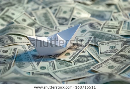 Origami paper boat at sea of money / studio photography of american moneys of hundred dollar on background