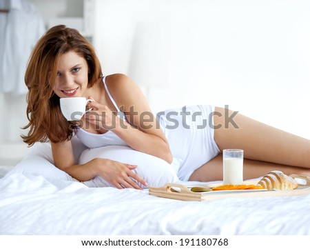 Drinking tea before bed? / smiling young girl lying in bed with white porcelain cup