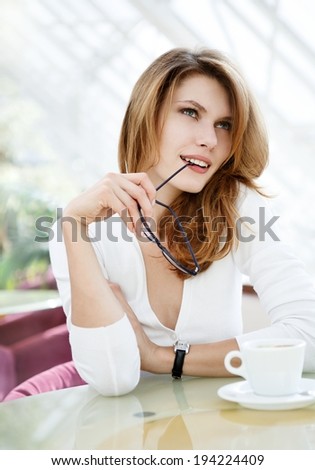 Brunette bites on her glasses earpiece looking up / photo of beautiful woman sitting in a coffee house