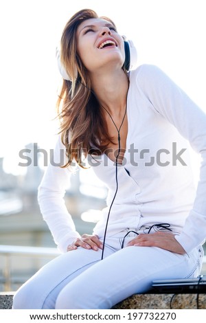 Captivating young girl listens to music through headphones / smiling brunette girl in white clothes with white headphones looking to the sky