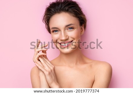 Beautiful woman applying moisturizer cream on her hands. Photo of smiling woman with perfect makeup on pink background. Beauty concept