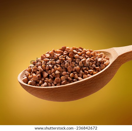 Roasted buckwheat in a wooden spoon / cereal on wooden spoons isolated on golden background