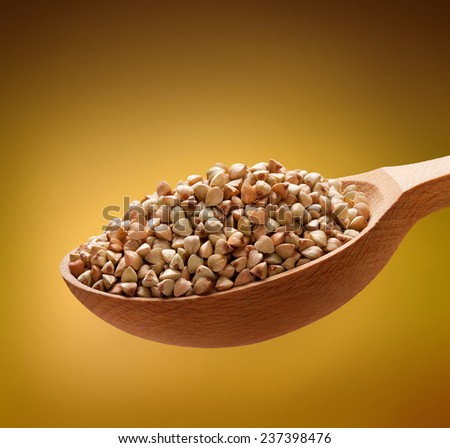 Buckwheat groats in a wooden spoon / cereal on wooden spoons isolated on golden background