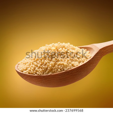 Couscous (cooking) in a wooden spoon / cereal on wooden spoons isolated on golden background