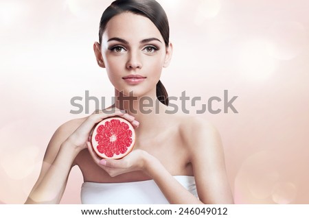 Young woman with grapefruit cut in half, healthy life concept / photoset of attractive girl holding a cut piece of pomelo in her hands - on blurred beige bokeh background