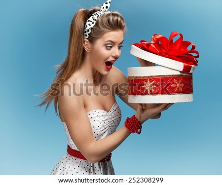 Excited birthday girl opening surprise gift with a look of amazement and shock / set photos of beautiful young retro pinup woman on blue background