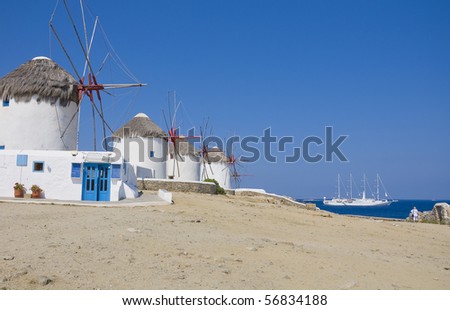 A number of windmills on a hillside on the island of Mykonos and a ship at sea - the main and most famous place on the island...