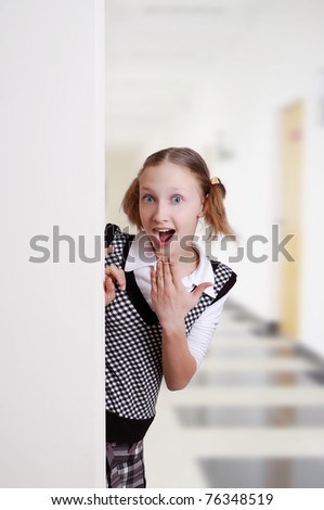 Schoolgirl peeks from behind the wall of school corridor