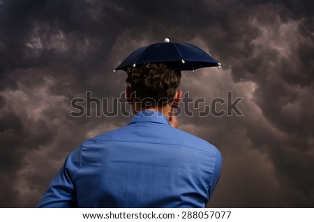 Business man with small umbrella in front of a heavy storm