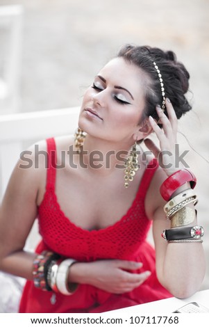 Beautiful young woman in red dress sits at little table in cafe