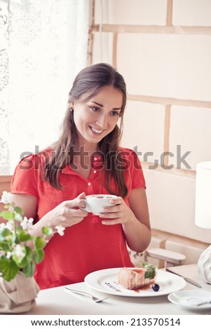 Pretty brunette young woman with cup of cappuccino in the cozy cafe