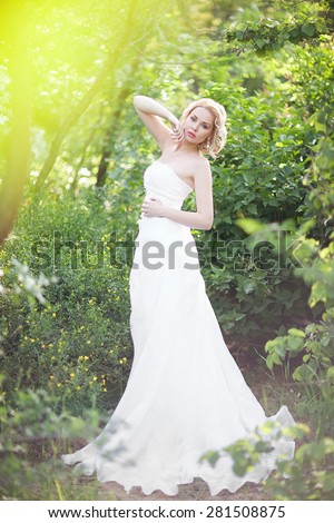 beautiful elegant bride with blond hair posing in the green forest