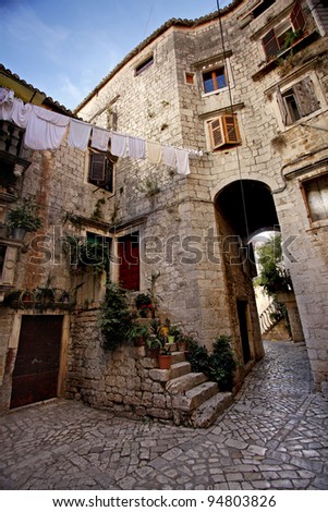 Narrow stone street of Trogir, with a scale that goes to an apartment and a stone arch and laundry to dry