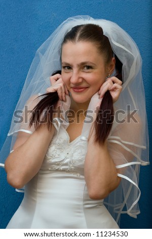 The cheerful bride in a white dress and a veil keeps tail of hair in her hands