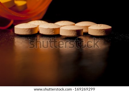 Pills Poured Out on a dark table next to pill bottle.