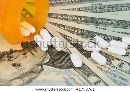 Spilled prescription pills on a fanned out stack of twenty dollar bills.