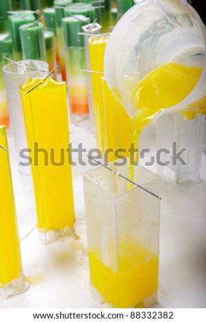 Candle manufacture , pouring colorful molten yellow wax into plastic moulds