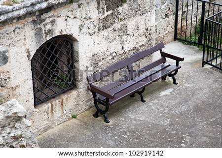 Lonely bench next to window with metal grate
