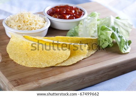 Taco ingredients: taco sauce, lettuce, taco shells and shredded cheese.