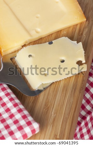 Block of cheese with cheese slicer and slice of cheese on cutting board.