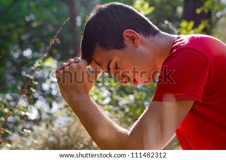 Young man kneeling and praying in forest