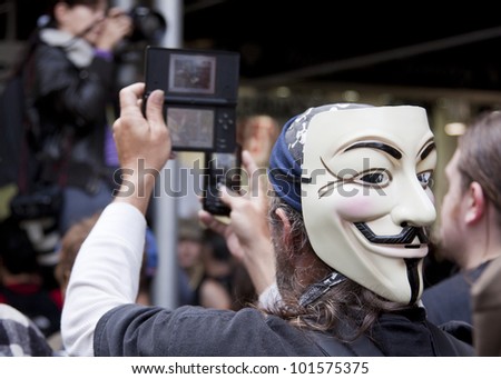 NEW YORK - MAY 1: A protester wearing a Guy Fawkes mask records the march to Union Square from Bryant Park on two mobile devices at Occupy Wall St \'May Day\' protests on May 1, 2012 in New York, NY.