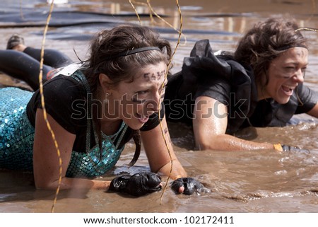 POCONO MANOR, PA - APR 28: Two women crawl through water under electrified wires at Tough Mudder event on April 28, 2012 in Pocono Manor, Pennsylvania. The course is designed by British Royal troops.