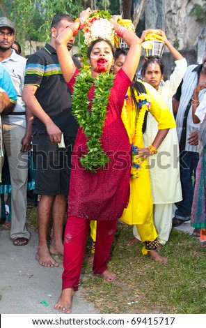 BATU CAVE, MALAYSIA - JAN 20 : Woman carrying big pot of milk with her tongue pierced during Thaipusam on January 20, 2011 at Batu Cave temple, Malaysia.