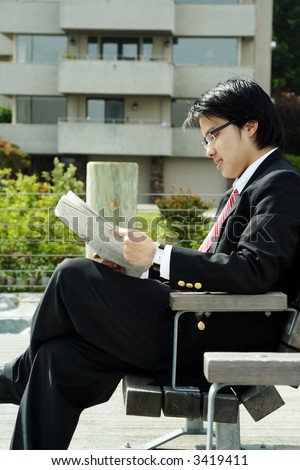 A businessman reading a newspaper on the bench outdoor