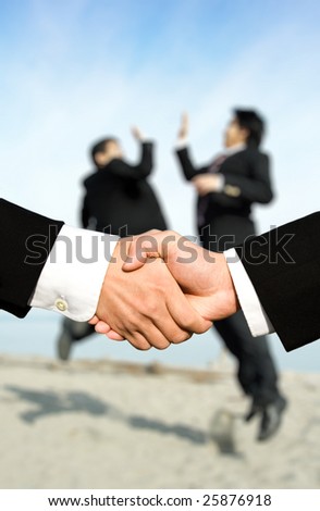 Two businessmen shaking hands with other two businessmen celebrating in the background, can be used for success concept