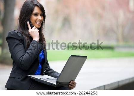 A shot of an indian businesswoman talking on the phone and working on her laptop outdoor