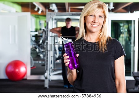 A shot of a happy caucasian female athlete holding a water bottle in a gym