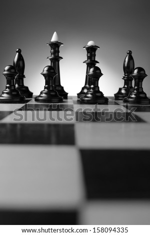 Low angle view of a line of backlit chess pieces on a chessboard with pawns, king , queen and bishops