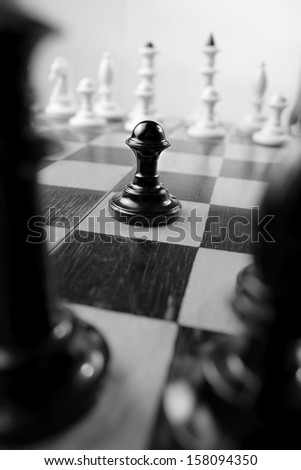 Low angle view between two chess pieces of a black pawn on a chessboard with the white pieces lined up in the background in this game of strategy and skill