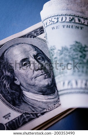 Detail of a US 100 dollar bill with notes on top of the stack folded back to reveal the portrait of statesman Benjamin Franklin, vertical format on a blue background