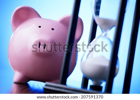 Close-up of a pink porcelain piggy bank with a vintage hourglass behind, concept of saving money and passing time