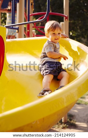 Little boy playing in a kids playground sliding round a colorful yellow circular slide with a happy smile