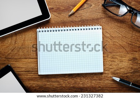 Close up Blank Graphing Notebook on Wooden Desk with Copy Space for Text, Surrounded with Gadgets, Pen, Pencil and Eyeglasses.