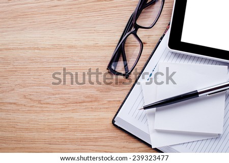 Glasses, pen, cell phone,notebook lie on light brown desktop