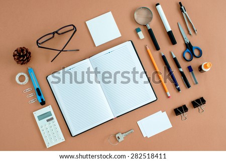 Assortment of Office Supplies Neatly Organized Around Note Book Open to Blank Page on Desk Top Surface