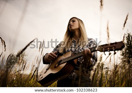 Young attractive blonde with a guitar on meadow