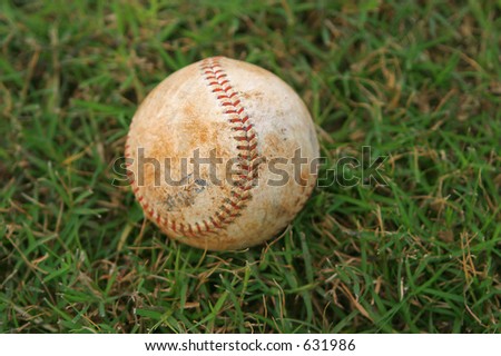 One Single Dirty baseball in green grass on baseball field